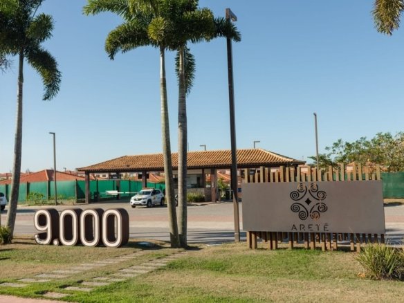 Acesso ao Aretê com placa, número 9.000, palmeiras e edificações ao fundo.