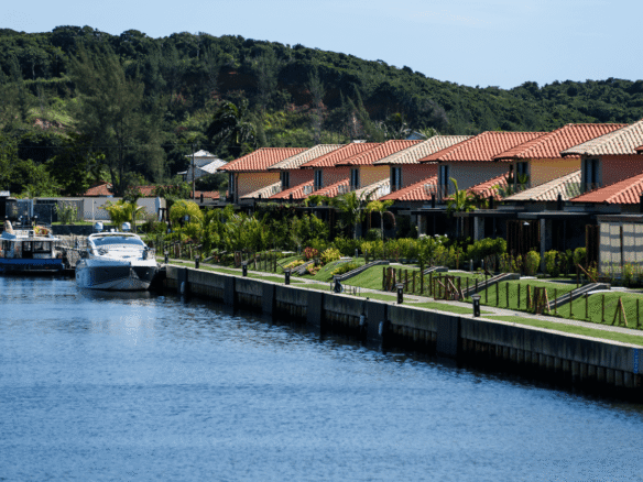 Canal com embarcação atracada diante de uma sequência de casas e jardins.