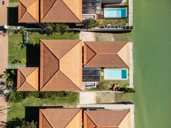 Vista aérea vertical de casas com jardins e piscinas junto ao canal.