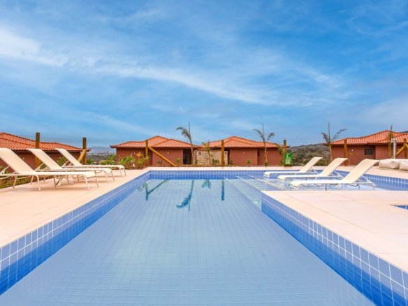 Piscina do condomínio Alto Ybirá, com espreguiçadeiras na borda e as casas ao fundo (foto real)