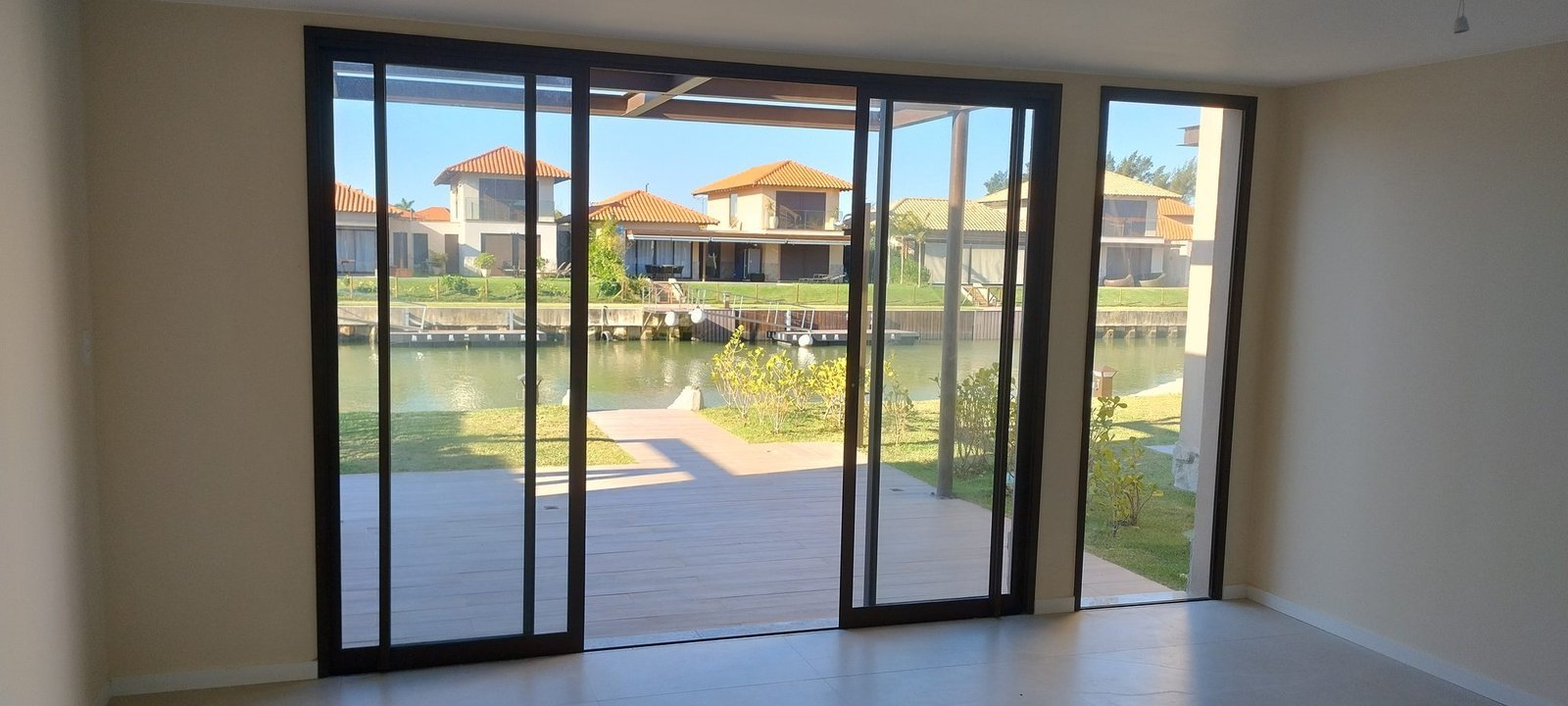 phoco-sync-30e4a92363fe6fdd-eb0cc470b037 Ambiente sem móveis de uma casa do Toriba Sul, com portas de vidro e vista para o canal e as casas da outra margem (foto real)