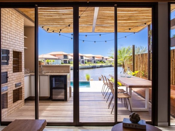 Área gourmet decorada da casa 10 do Condomínio B do Toriba Norte, com churrasqueira e portas de vidro abertas para o deck e o canal (foto real)