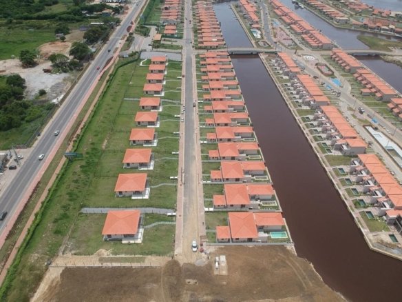 Vista aérea de um canal do Toriba entre duas fileiras de casas, com a estrada à esquerda (foto real)