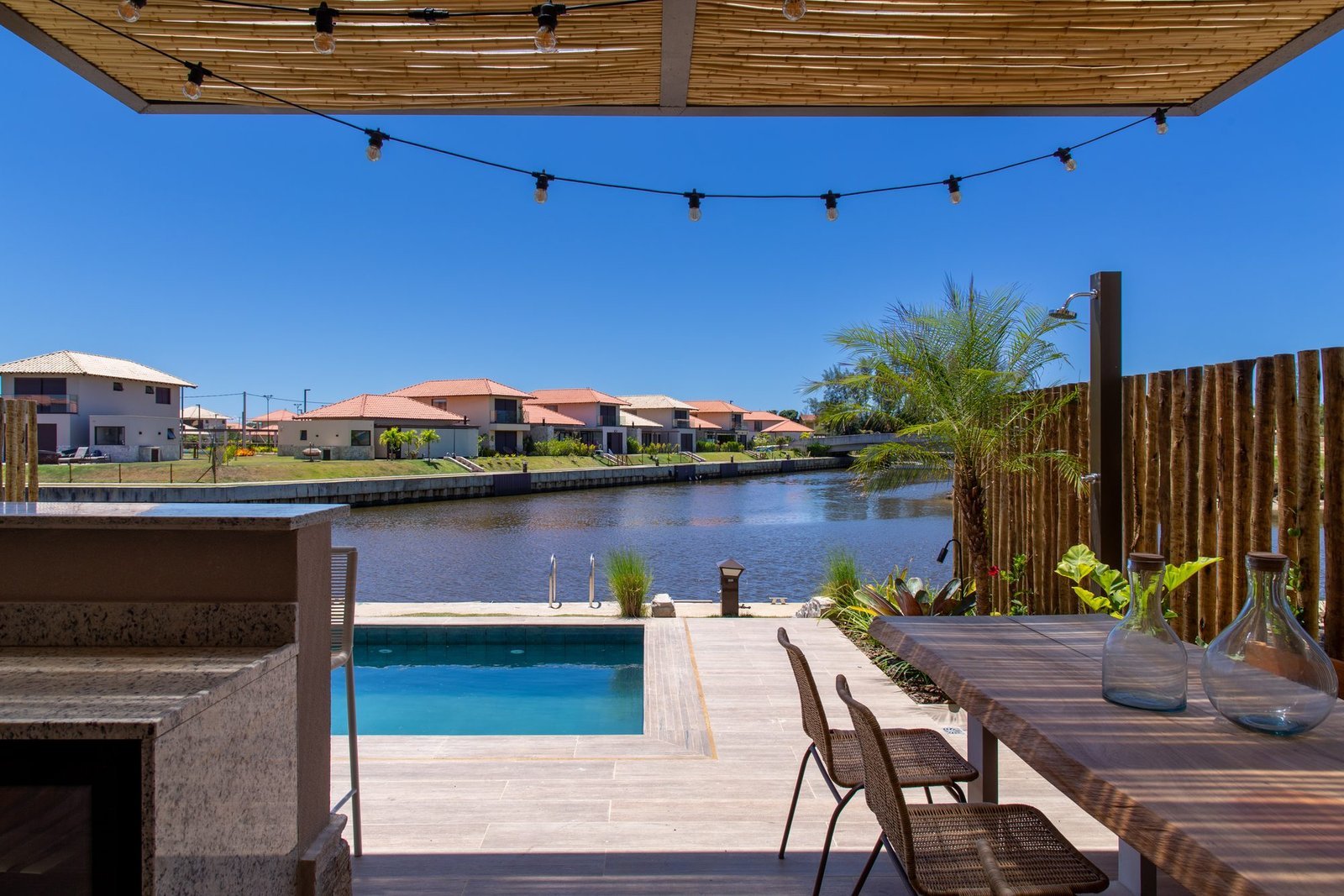 Varanda da casa 10 do Condomínio B do Toriba Norte, decorada, com mesa, piscina e o canal ao fundo (foto real)