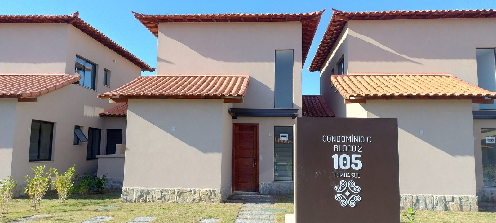 phoco-sync-c7364d02b1879b83-3eafb4620eef Frente de uma casa do Condomínio C do Toriba Sul, com a placa de identificação da casa e o jardim (foto real)