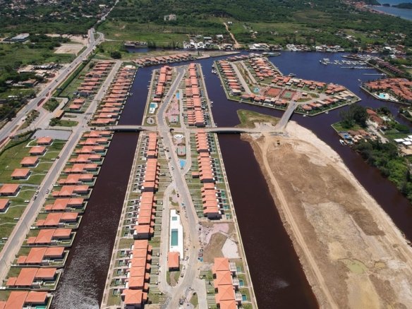 Vista aérea dos canais do Toriba, com fileiras de casas nas margens, uma ponte e uma área ainda sem casas à direita (foto real)