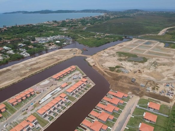 Vista aérea de um canal do Toriba, com casas à margem, áreas ainda sem casas e o mar ao fundo (foto real)