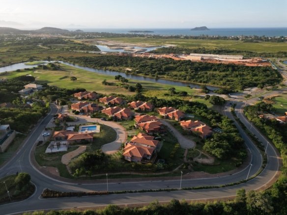 Vista aérea do condomínio Alto Ybirá em maio de 2026, com as casas e a piscina entre a estrada e o campo de golfe, e o mar ao fundo (foto real)