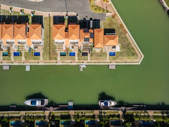 Vista aérea de casas no Toriba, com telhados, piscinas, jardins e canal.
